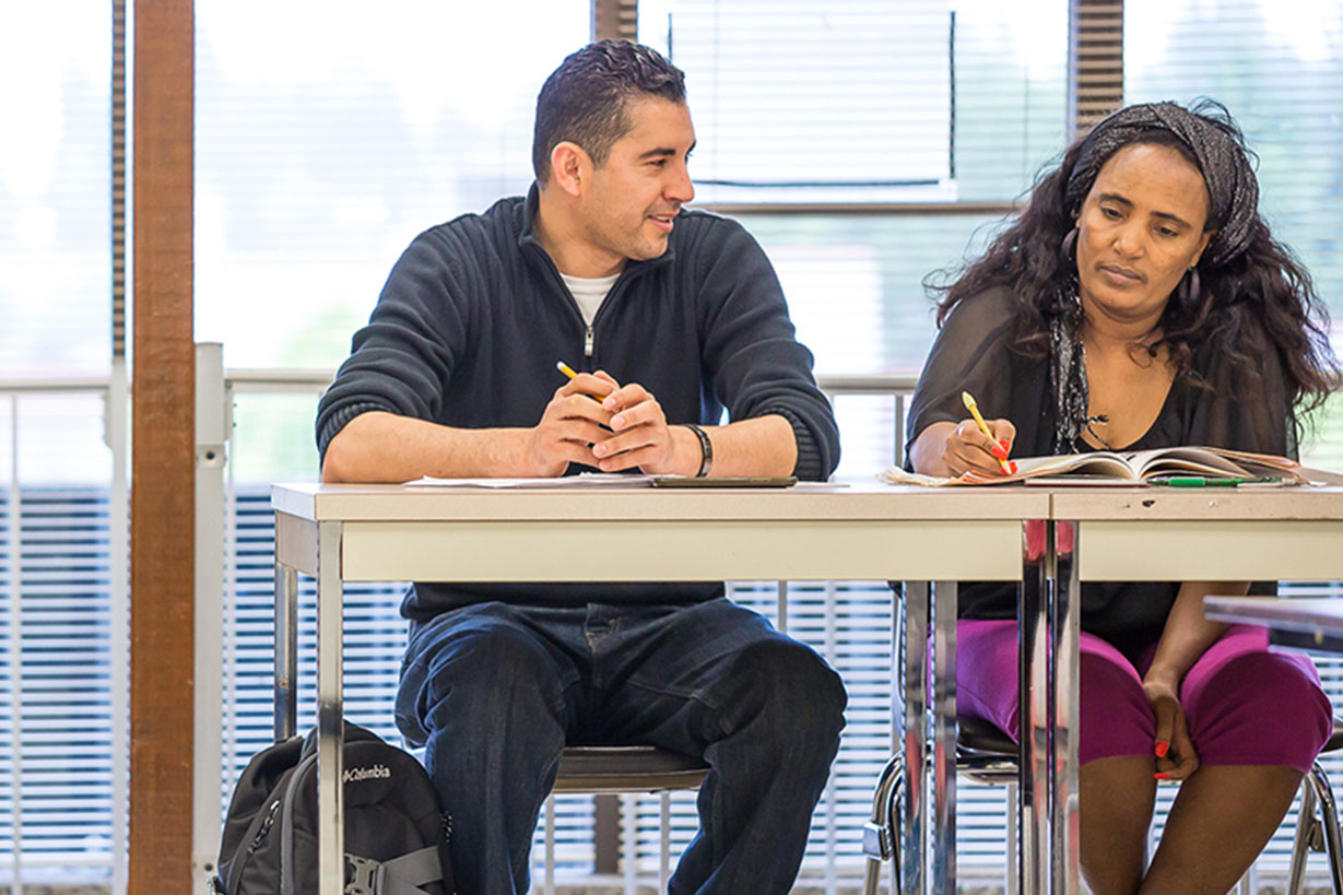 2 students sit next to each other with books open.