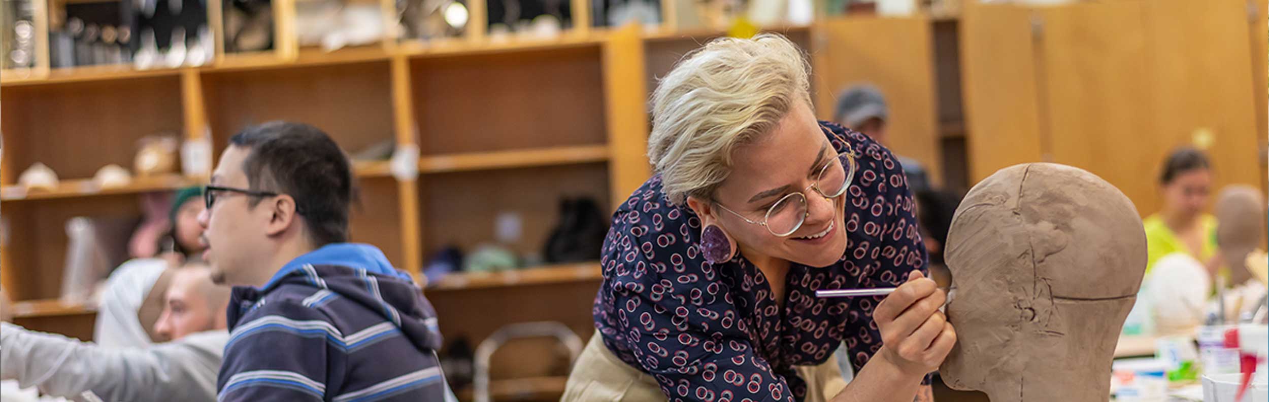  Female student sculpting a clay head in a classroom 