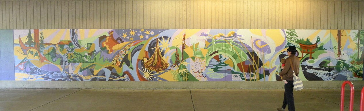 A student wearing a hat and bag standing in front of a mural.